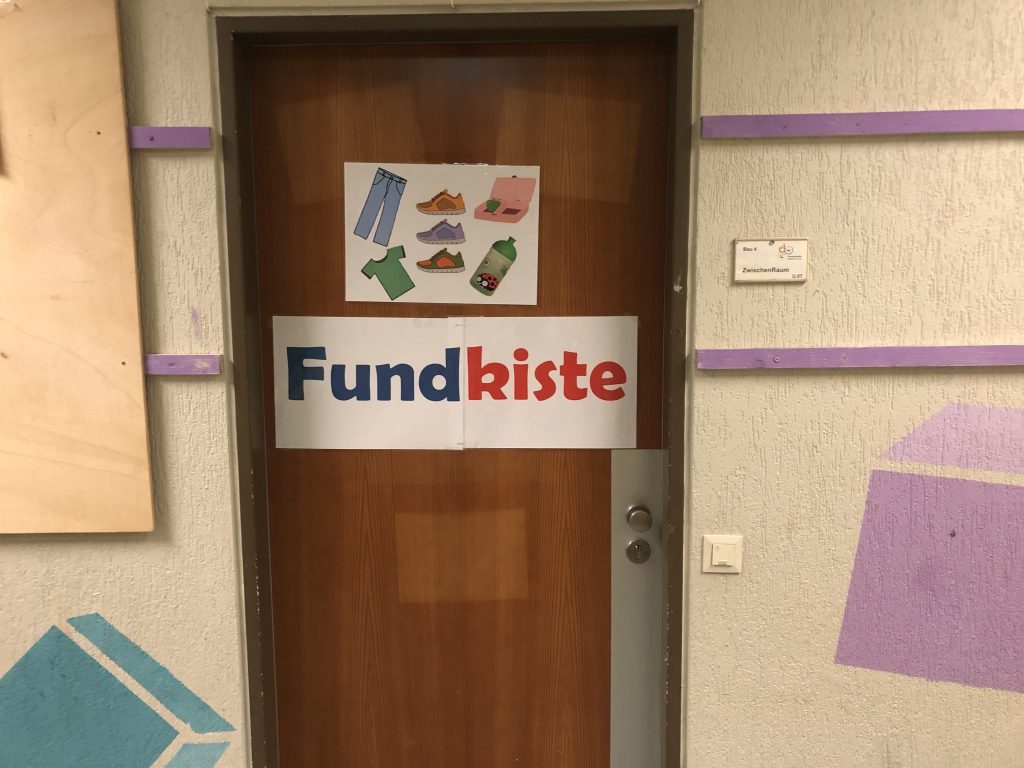 Die Fundkiste der Grundschule für Anziehsachen, Brotdosen, Regenschirme und Ähnliches ist umgezogen. Sie befindet sich nun im unteren Stockwerk auf der linken Seite. Wir schließen Ihren Kindern und Ihnen gerne auf, um einmal durchzuschauen, ob ein Fundstück wieder seine Besitzerin/ seinen Besitzer findet.